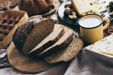 Leaves of bread lying on beige background with a yellow stylish cup of milk and a black dish of cheese with holes and nuts. Perfect for breakfast or brunch for healthy-food lovers.