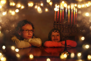 Low key image of jewish holiday Hanukkah background with two cute kids looking at menorah (traditional candelabra) and burning candles © tomertu