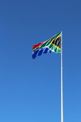 A South African flag on a flagpole with a blue sky background.