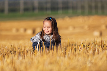 Happy 2 year old girl walking in a summer harvested field