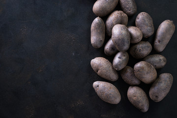 Raw potato food . Fresh blue potatoes on dark background. Free place for text.