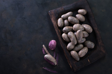 Raw potato food . Fresh blue potatoes on dark background. Free place for text.
