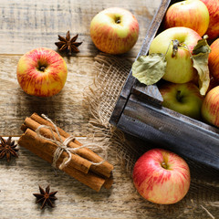 Box with ripe apples and cinnamom on wooden background