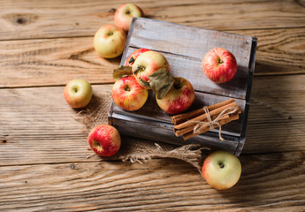 Box with ripe apples and cinnamom on wooden background
