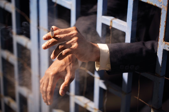 hands of businessman smoking cigarette in jail