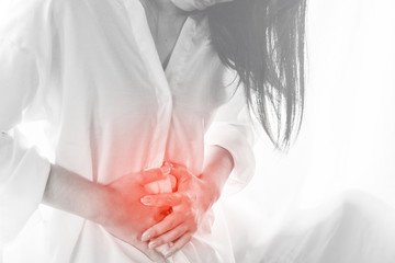 Asian woman standing against window with hand touching her stomach pain 