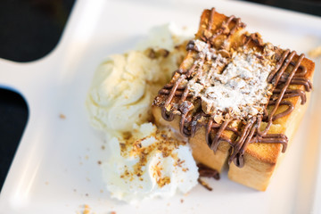 The toast bread topped with chocolate & almonds, whipped cream and vanilla ice cream serve on white dish for dessert background or texture.