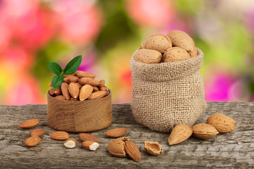 Almonds with leaf in bag from sacking on a wooden table with blurred garden background