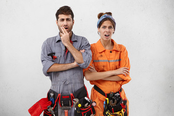 Discontent handyman and his female partner look at object they should repair, realize all difficulties, don`t know how to start reconstruction. Exhausted manual workers have displeased expressions