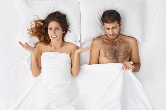 Indoor shot of upset female in bed shrugging shoulders in confusion, worrying about her husband who is suffering from impotence but keeps trying to do his best and be able to perform sexually