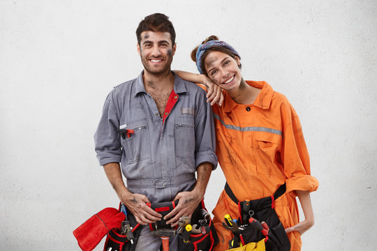 Smiling dirty woman leans on shoulder of man mechanic, helps him to repair car on work station, rejoice their succeess, earned much money, work as friendly team. Repairing and renovation concept
