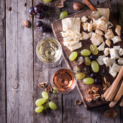 Different kinds of cheeses, wine, fruits and snacks on rustic wooden table . still life concept