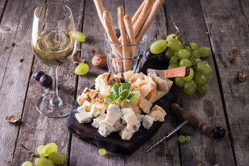 Different kinds of cheeses, wine, fruits and snacks on rustic wooden table . still life concept