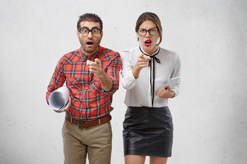 Scrupulous female and male enterpreneurs point at you and have wrathful or aroused look, being irritated after long work at project. Male nerd and pretty female see something strange in front