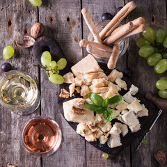 Different kinds of cheeses, wine, fruits and snacks on rustic wooden table . still life concept