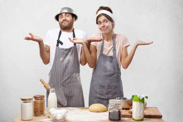 Uncertain young attractive female and her husband shrug shoulders, have bewilderment, don`t know...