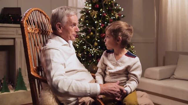 Cheerful loving elderly man presenting his grandson a Christmas present