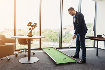 A man in a strict business suit plays in an office in a mini-golf