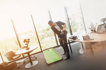 A man in a strict business suit plays in an office in a mini-golf