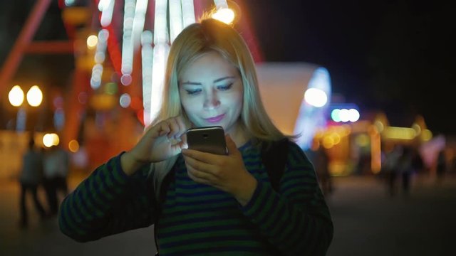 Blond hair young girl with mobile at late night park looks photos