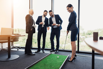 Three businessmen and business ladies play golf. A woman is holding a golf stick in the dots. Men...