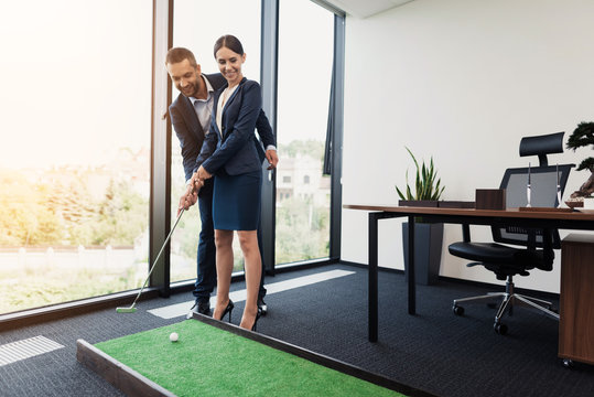 An Elderly Man Is Teaching His Secretary To Play Mini Golf. He Directs Her