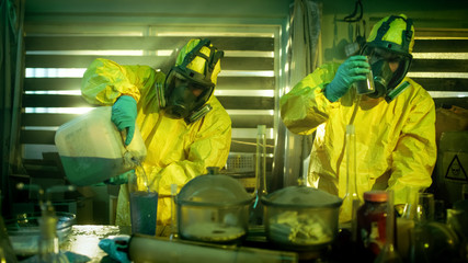 In the Underground Drug Laboratory Clandestine Chemists Wearing Protective Masks and Coveralls Mix...