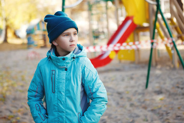 Girl in jacket and hat sad near the Playground, which is fenced around with tape. Baby safety
