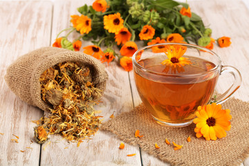 Calendula tea with fresh and dried flowers on white wooden background