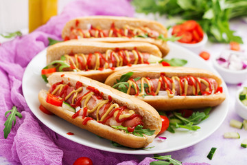 Hot dog with sausage. bacon, cucumber, tomato and red onion on white plate
