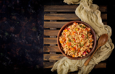 Vegetarian crumbly pearl barley porridge with vegetables  in a dark background. Flat lay. Top view