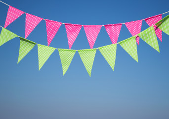 garlands with multi-colored flags against a background of blue sky. garland of green and  pink  flags. festive background. Party flags decoration on outdoor.