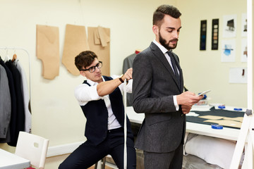 Portrait of handsome young man being fitted in bespoke suit by tailor in traditional atelier studio