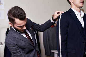 Portrait of modern tailor measuring arm length of bespoke suit during model fitting in traditional atelier studio