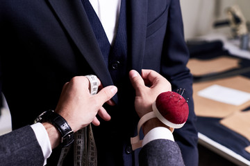 Closeup of tailor fitting bespoke suit to model, hands with tape measure and pin cushion fixing...