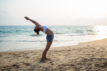 Natural looking pregnant woman practicing yoga at the seashore at sunset