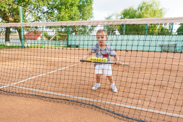 Little cute kid playing tennis outside at the tennis court