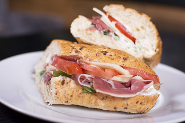 Fresh sandwich with ham, cheese, bacon, tomatoes, lettuce, cucumbers and onions on dark wooden background. Delicious restaurant meal.