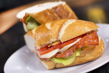 Fresh sandwich with ham, cheese, bacon, tomatoes, lettuce, cucumbers and onions on dark wooden background. Delicious restaurant meal.