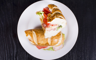 Fresh sandwich with ham, cheese, bacon, tomatoes, lettuce, cucumbers and onions on dark wooden background. Delicious restaurant meal.