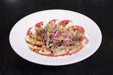 Delicious salad, prosciutto, and mozzarella cheese over dark background. Close up view of a delicious restaurant meal.