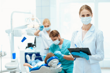 Naklejka na ściany i meble A nurse posing against a background of dentists who treat a girl's teeth. She is wearing a medical mask