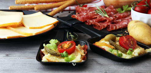 Delicious traditional Swiss melted raclette cheese on diced boiled or baked potato served in individual skillets with salami..