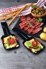 Delicious traditional Swiss melted raclette cheese on diced boiled or baked potato served in individual skillets with salami..