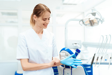 Female dentist posing against a background of dental equipment in a dental clinic. She puts on gloves