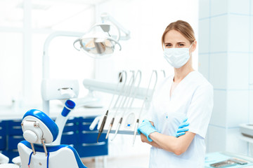 Female dentist posing against a background of dental equipment in a dental clinic. She is posing in a medical mask