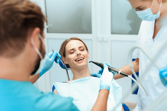A woman is sitting in a dental chair, doctors dentists bent over her