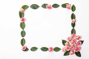 Round frame made of pink and beige roses, green leaves, branches, floral pattern on white background. Flat lay, top view. Valentine's background