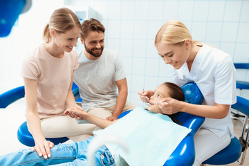 Obraz premium Parents brought their daughter to see a dentist. The girl is sitting in the dental chair. A doctor stands nearby