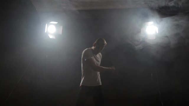 guy dancing in the dark in the backlight. a young man rhythmically moves his arms